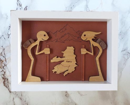 Framed layered wooden art featuring Kerry walkers with map and mountain backdrop - precision-cut walnut, plywood and clear acrylic hiking sculpture in white frame