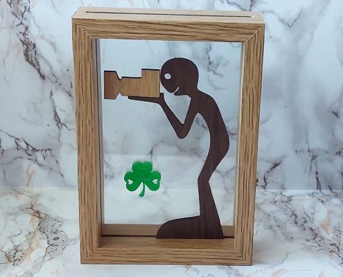 Framed wooden art featuring boy photographer with plywood camera and green acrylic shamrock - walnut and acrylic Irish-themed decor
